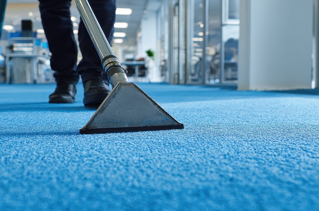 Ein Fachmann reinigt einen blauen Teppich in einem modernen Büro mit einem industriellen Dampfreiniger mit Absaugvorrichtung