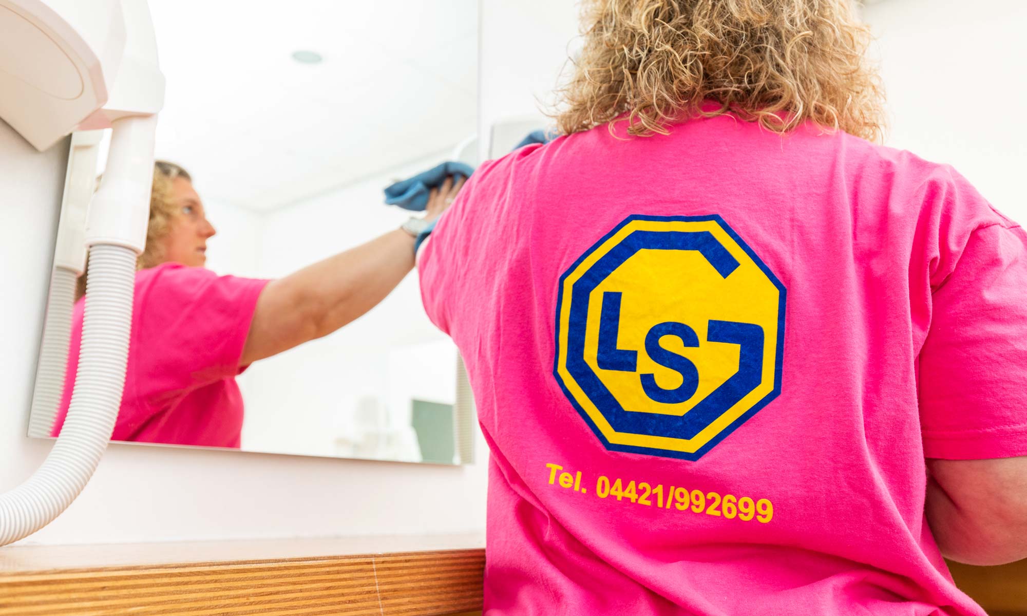 Person mit neutralem Ausdruck in pinkem Shirt mit blau gelbem Logo