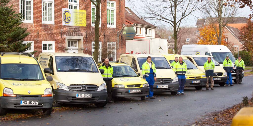 Fuenf Personen laechelnd vor gelben Dienstwagen in Neonwesten am Strassenrand