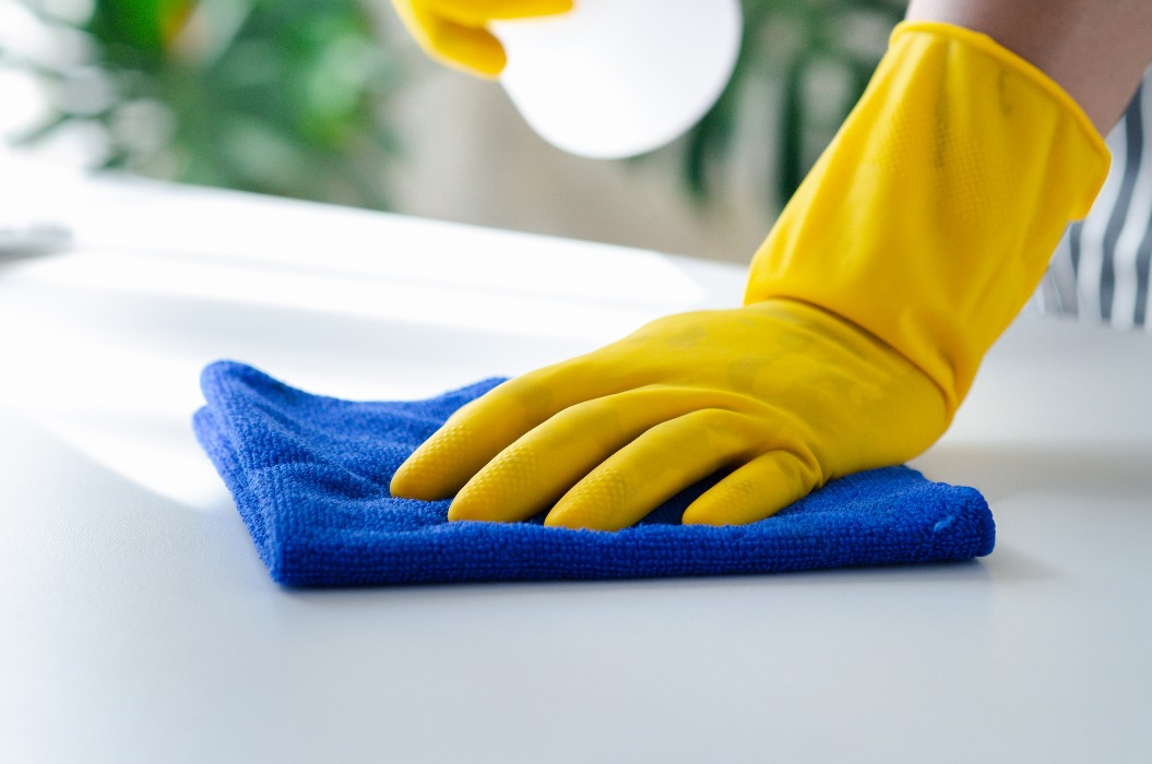 Eine Person, die den Raum reinigt; das Reinigungspersonal wischt die Tische im Büro der Firma mit einem Tuch ab und sprüht Desinfektionsmittel auf. Reinigungspersonal. Gewährleistung der Sauberkeit im Unternehmen.