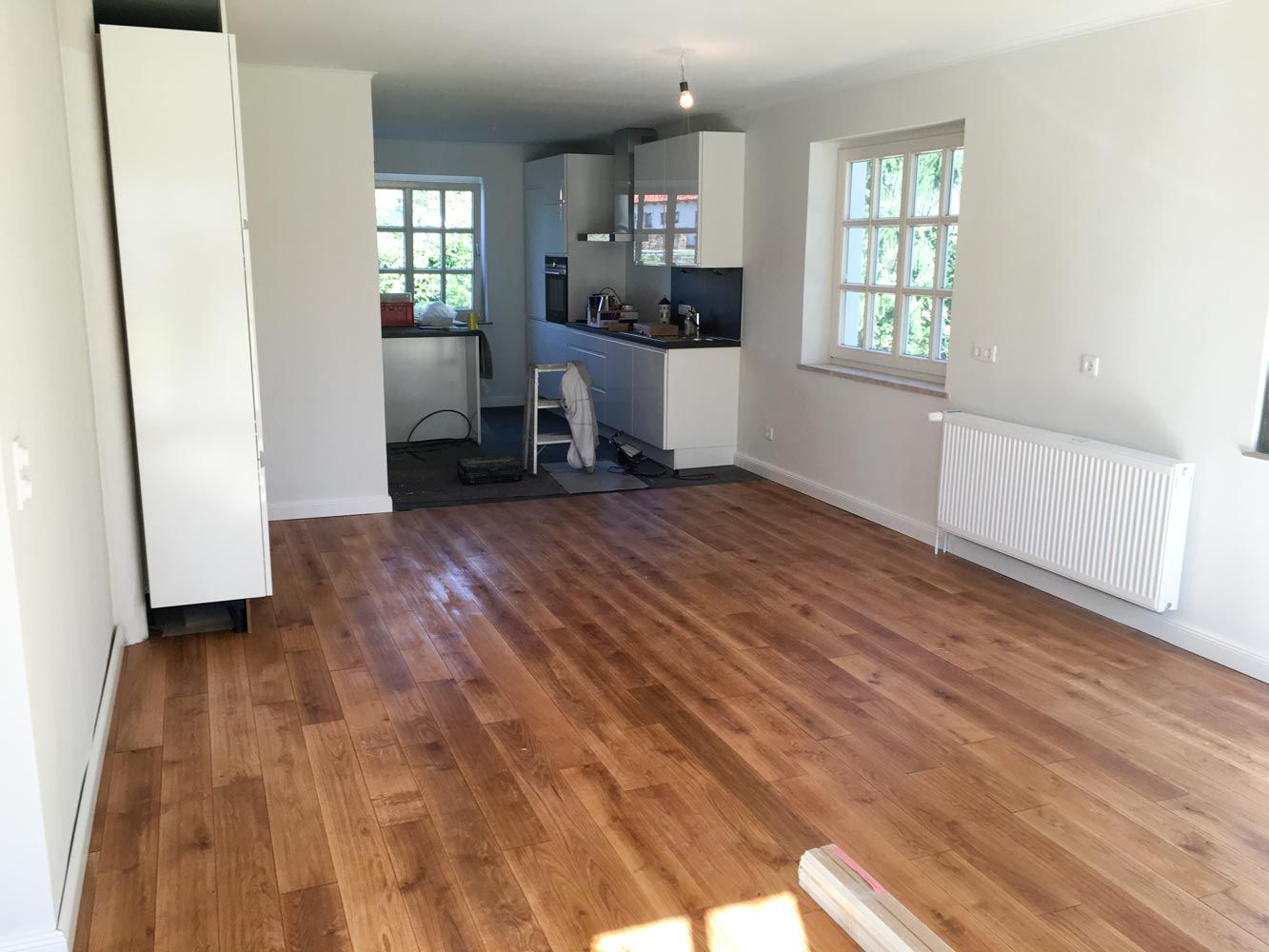Leerer Raum mit Holzboden weisser Kueche und Fenstern waehrend Renovierung