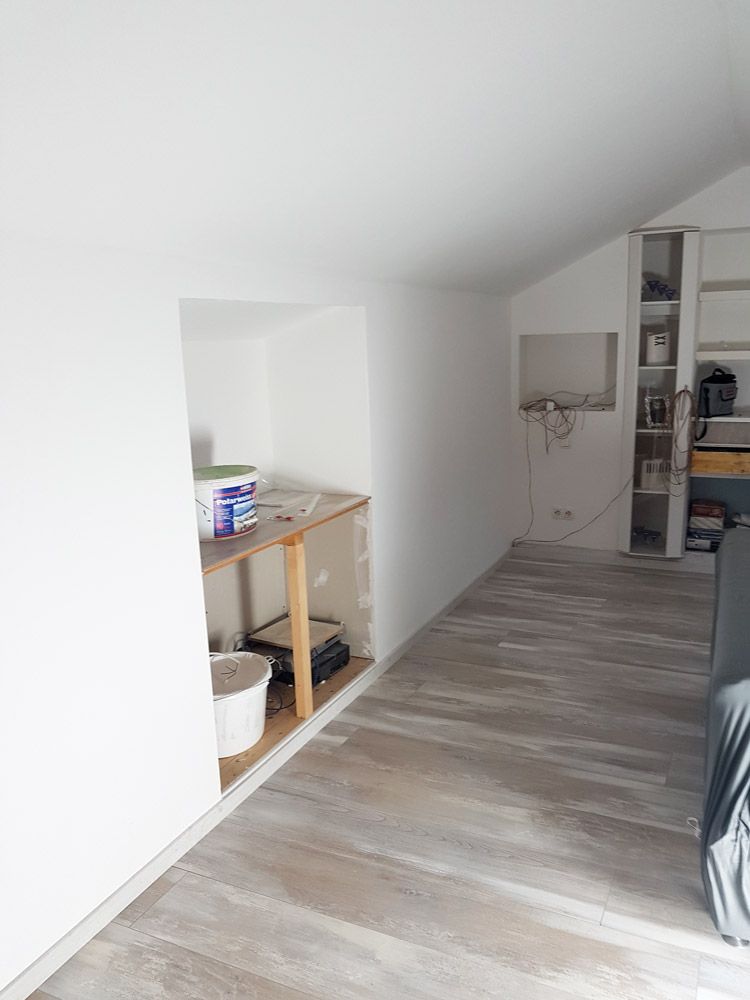 Renovierungsraum mit weissen Waenden Farbeimern und hellem Holzboden