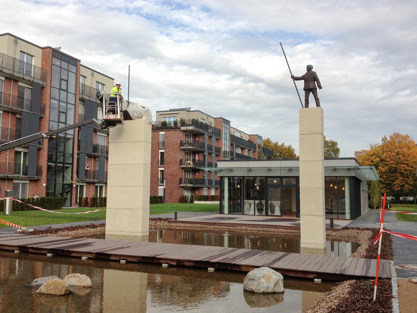 Ein Arbeiter in Warnweste installiert eine Bronzestatue auf einer Saeule