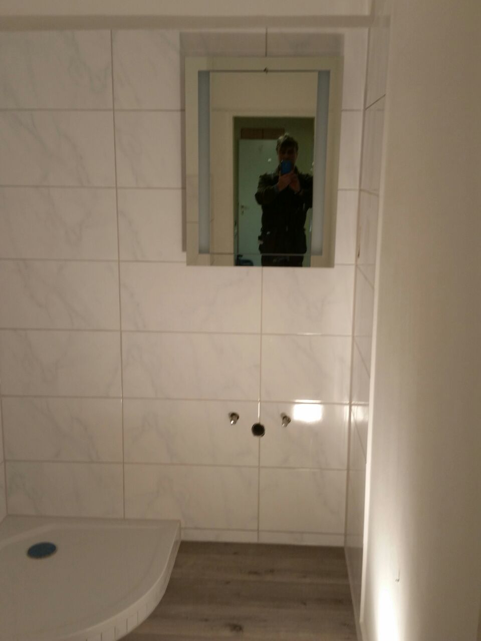Eine Person in dunkler Jacke fotografiert sich im Spiegel eines Badezimmers