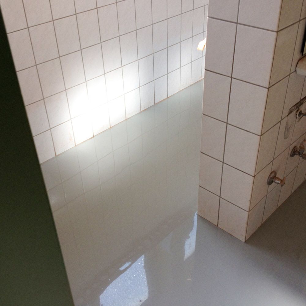 Weiss gekachelter Duschraum mit Wasserpfuetze und alten Armaturen an der Wand