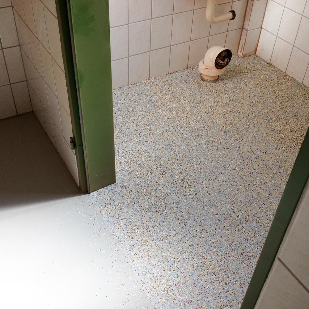 Renovierter Sanitaerraum mit gesprenkeltem Bodenbelag und weissen Fliesen