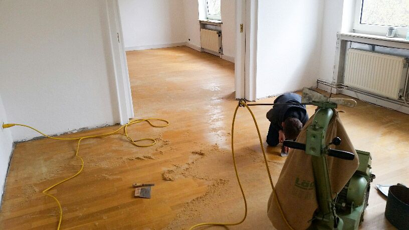 Ein Mann in dunkler Kleidung schleift konzentriert einen Holzboden ab