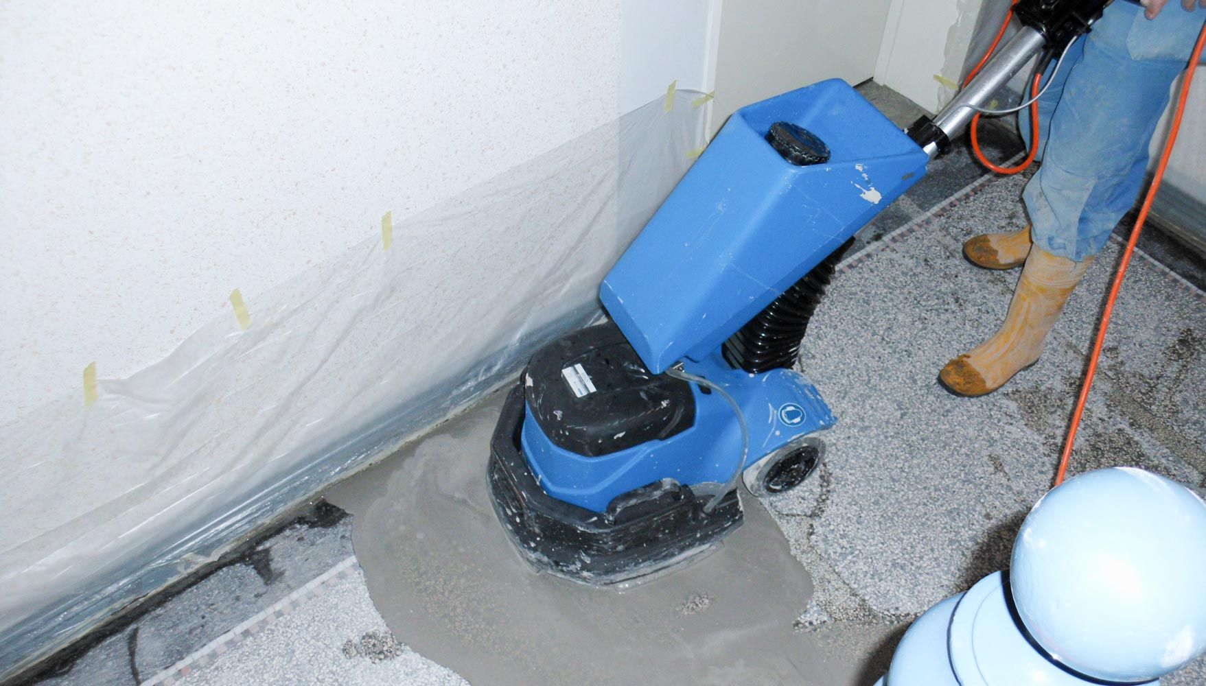 Ein Arbeiter in gelben Stiefeln bearbeitet einen Boden mit blauer Maschine