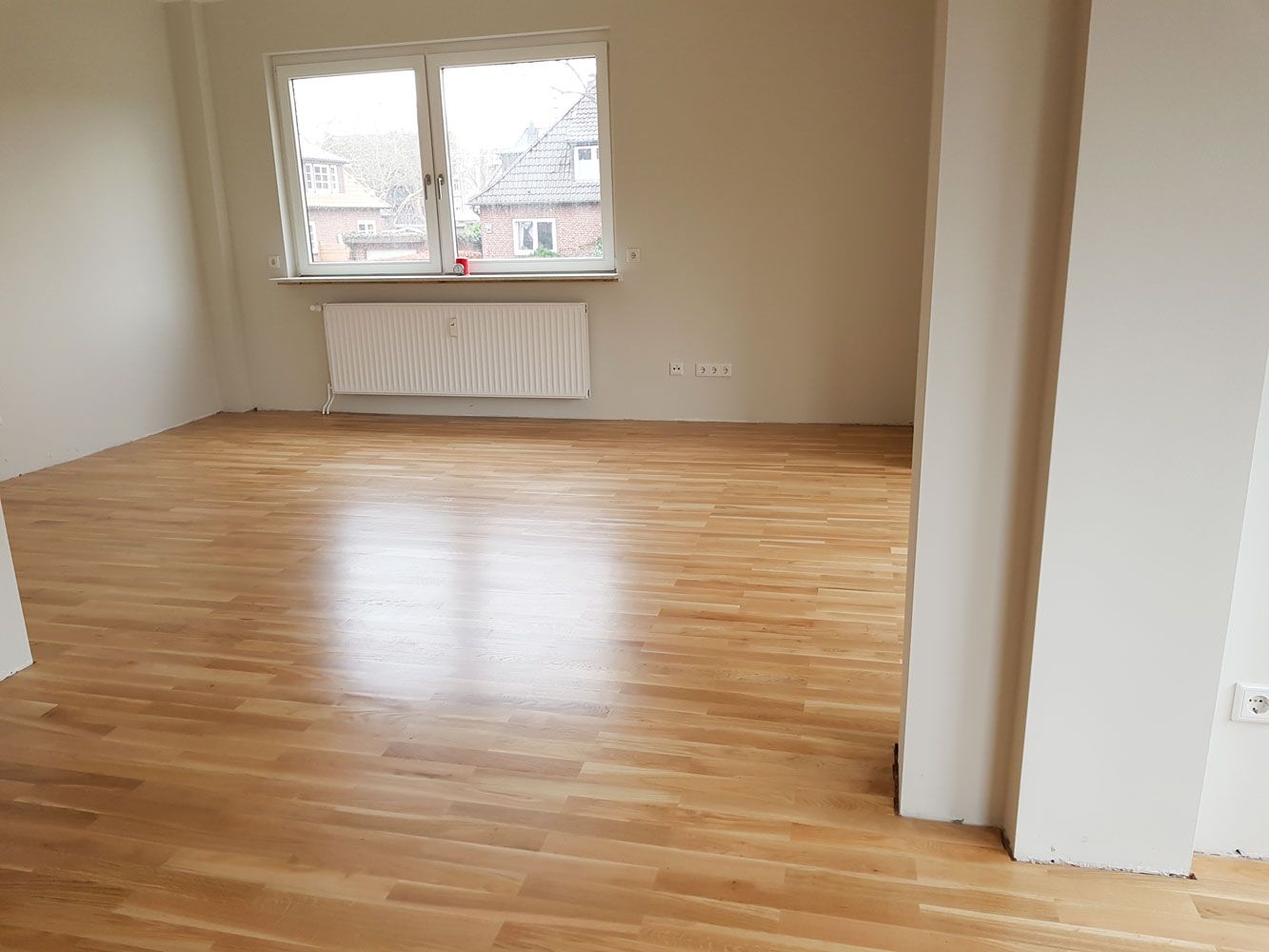 Leerer heller Raum mit glaenzendem Parkettboden Fenster und weisser Heizung