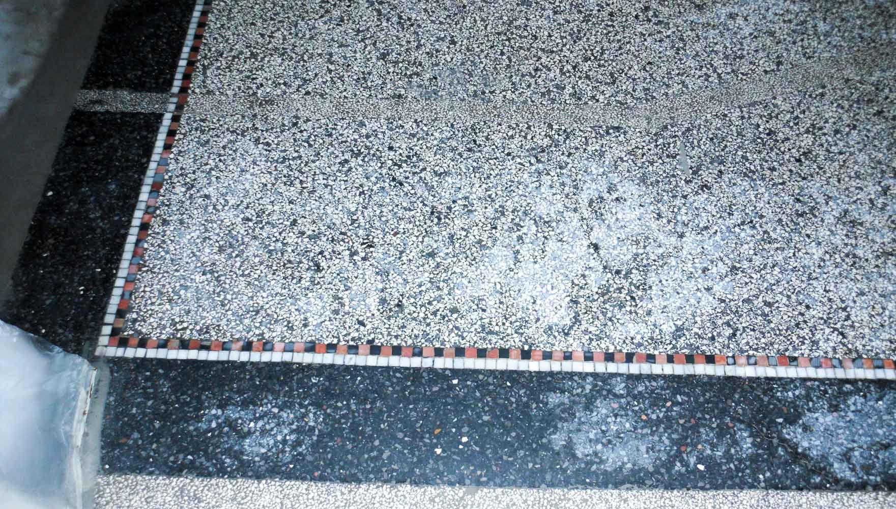 Grauer Terrazzoboden mit dekorativer roter und schwarzer Mosaikbordüre