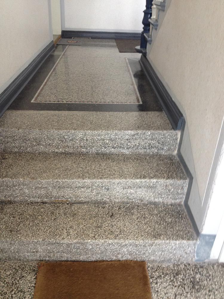 Ein grauer Terrazzo Treppenabsatz mit Fussmatten in einem hellen Hausflur